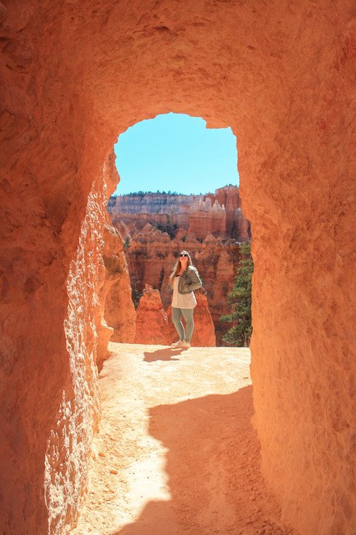 A hiker walking through a man-made tunnel carved into a red rock fin.