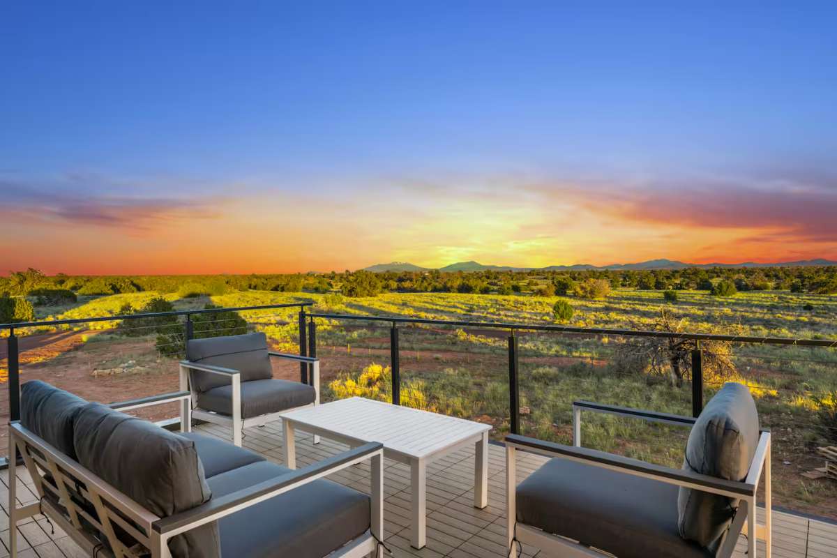 A wooden rooftop deck with chairs facing a vibrant sunset over a canyon landscape.