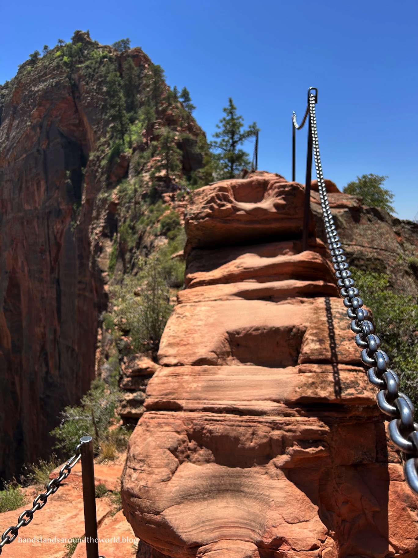 Hikers carefully navigating the narrow ridge and metal chains on the Angels Landing trail.